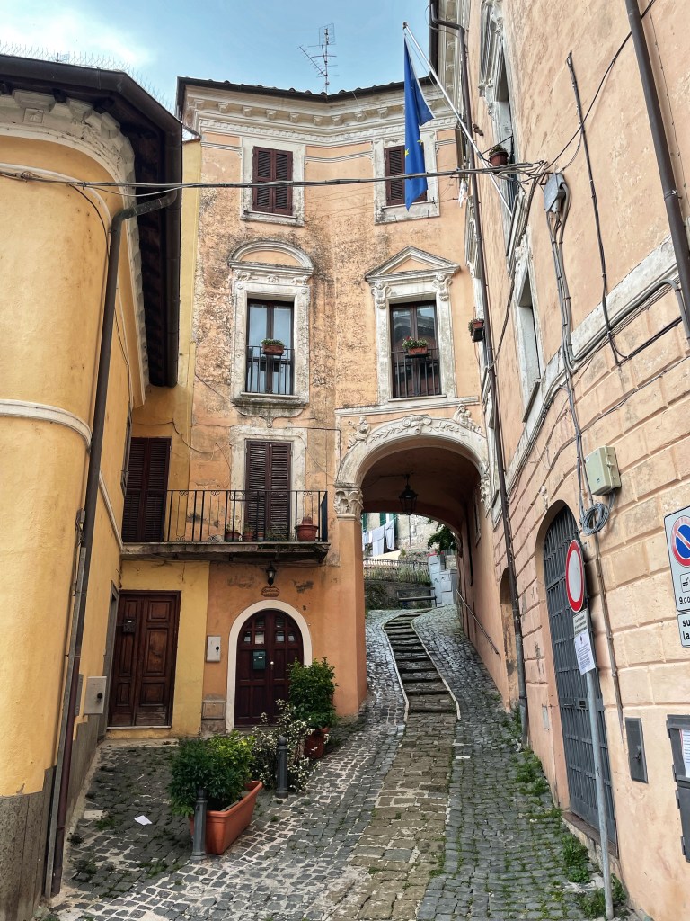 A cobble stone street that leads up a hill and under a arch that connects two old buildings. 